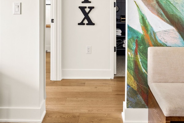 A glimpse into the hallway of a modern home, highlighting the light-colored hardwood flooring and crisp white walls. The space features a partial view of a vibrant mural, a built-in seating bench, and an inviting entryway into an adjacent room.