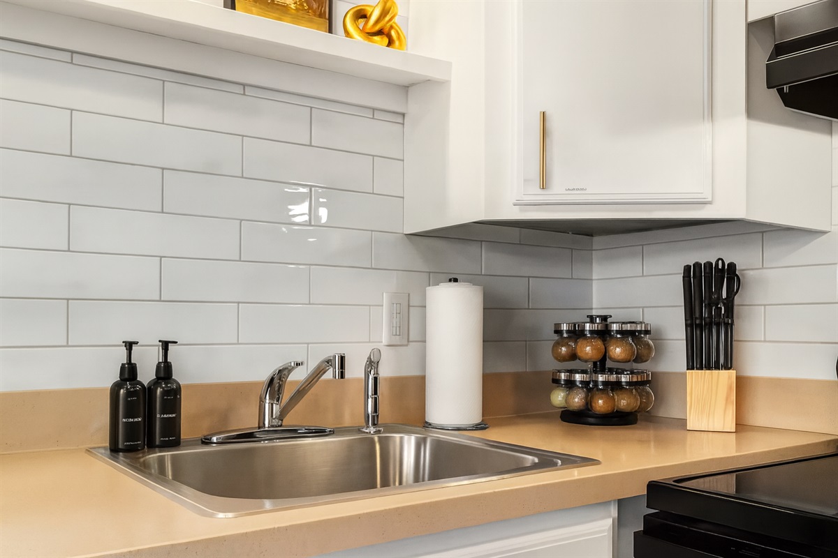 Modern kitchen with sleek countertops, subway tile backsplash, and fully stocked essentials including knives, spices, and cooking basics—perfect for enjoying home-cooked meals during your stay