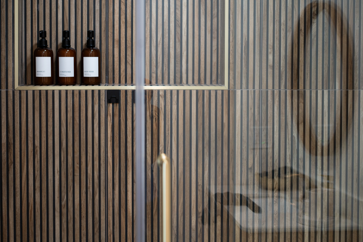 Amber glass toiletries, warm wood tile, and brass fixtures turn your morning shower into the best part of the day.