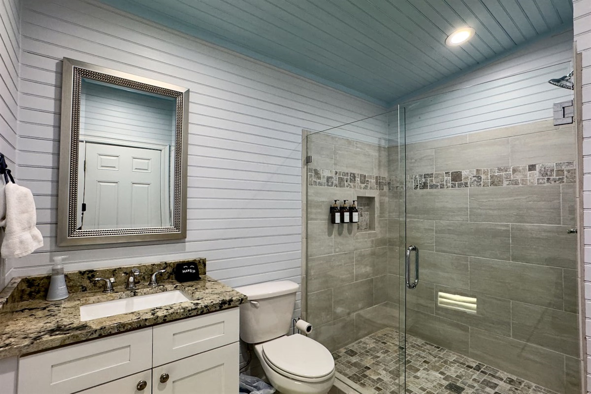 Stylish bathroom with a glass walk-in shower, granite vanity, and bright coastal design.