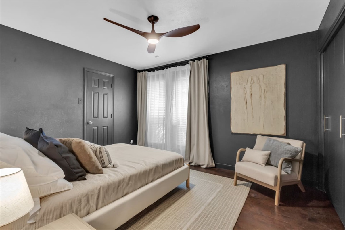 Guest bedroom with a queen bed, cozy sitting area, room-darkening shades, and a ceiling fan, providing a comfortable and restful space for your stay.
