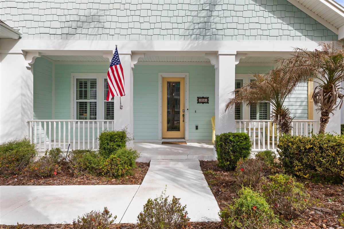 Follow the path to a breezy coastal welcome, where yellow porch rockers invite slow mornings, the pastel exterior sets the mood, and the first step to the door feels like the start of the easy beach getaway you’ve been needing.