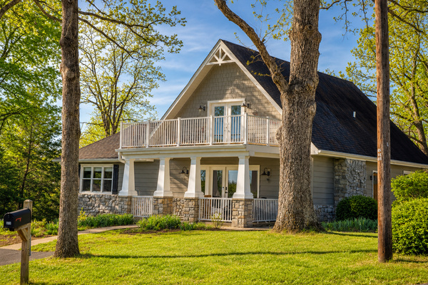 Welcoming front exterior with a covered porch, large yard and a peaceful wooded setting near the lake.