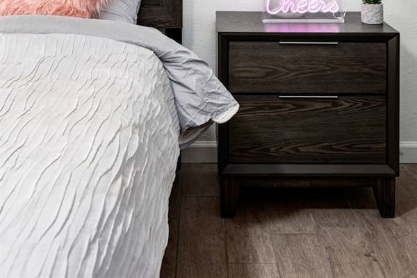 A glowing "Cheers" neon sign, elegant bedside lamp, and soft pink pillow create an inviting boutique-hotel feel.