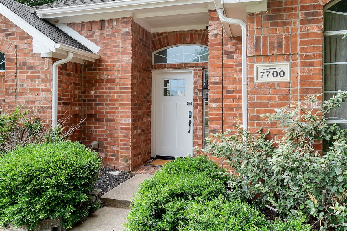 Welcome to our tranquil abode, where a keypad entrance beckons with ease, embraced by lush greenery all around.