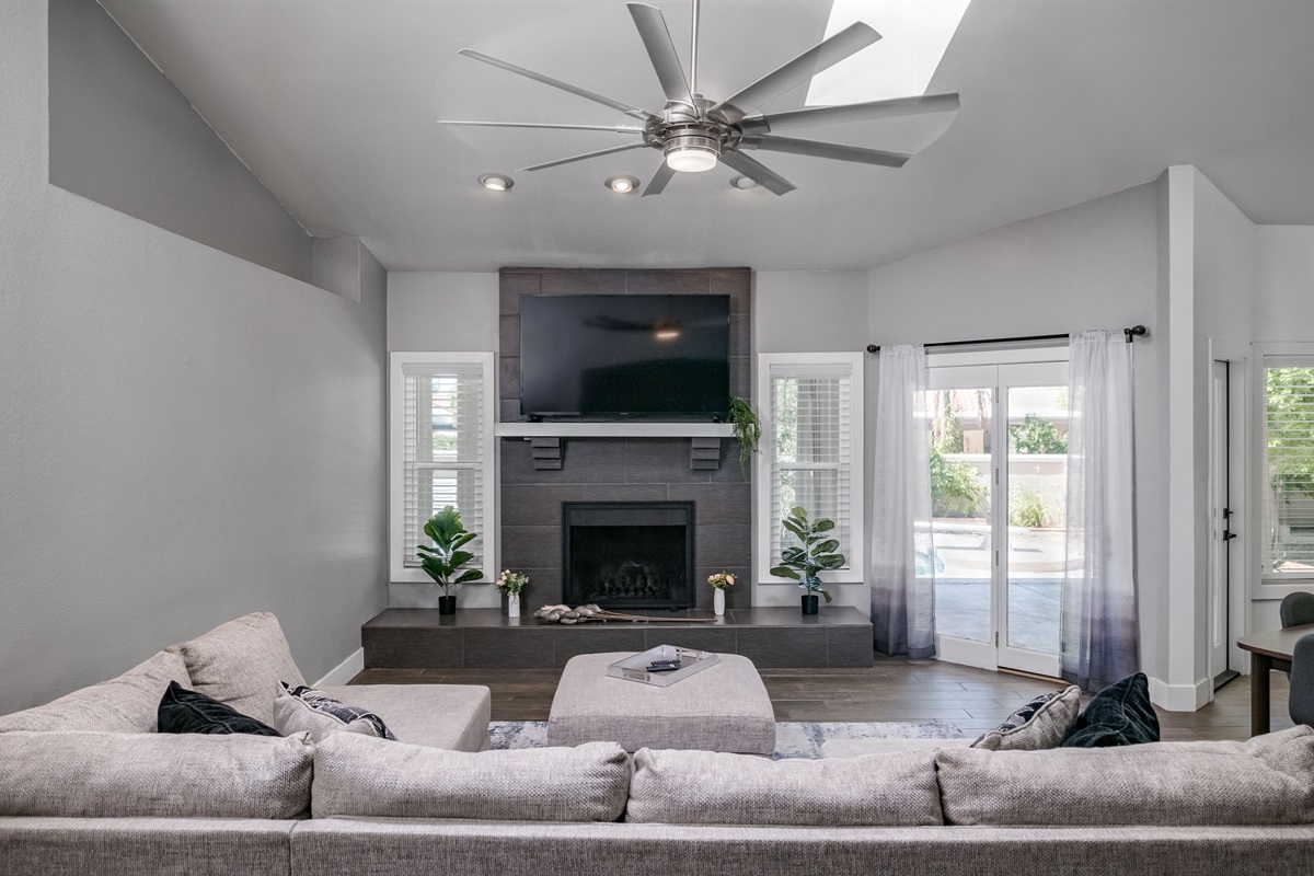 Spacious and sunlit, this living room features soaring ceilings, a cozy fireplace, and plenty of room for movie nights or game-day gatherings.
