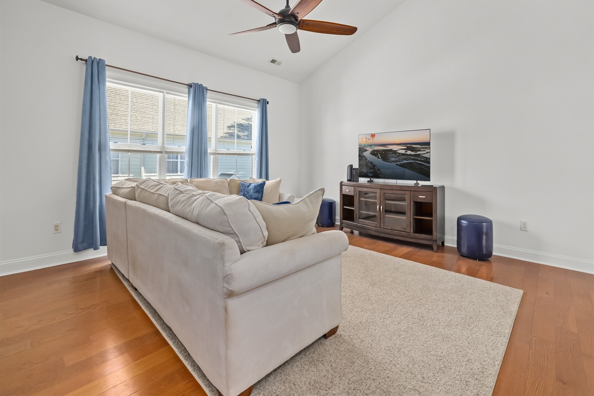 This airy, oversized living space is made for family movie nights, morning cartoons, afternoon naps, and late-night laughs. Vaulted ceilings and soft coastal light create a relaxed, open feel, while the generous sectional invites the whole crew to settle i