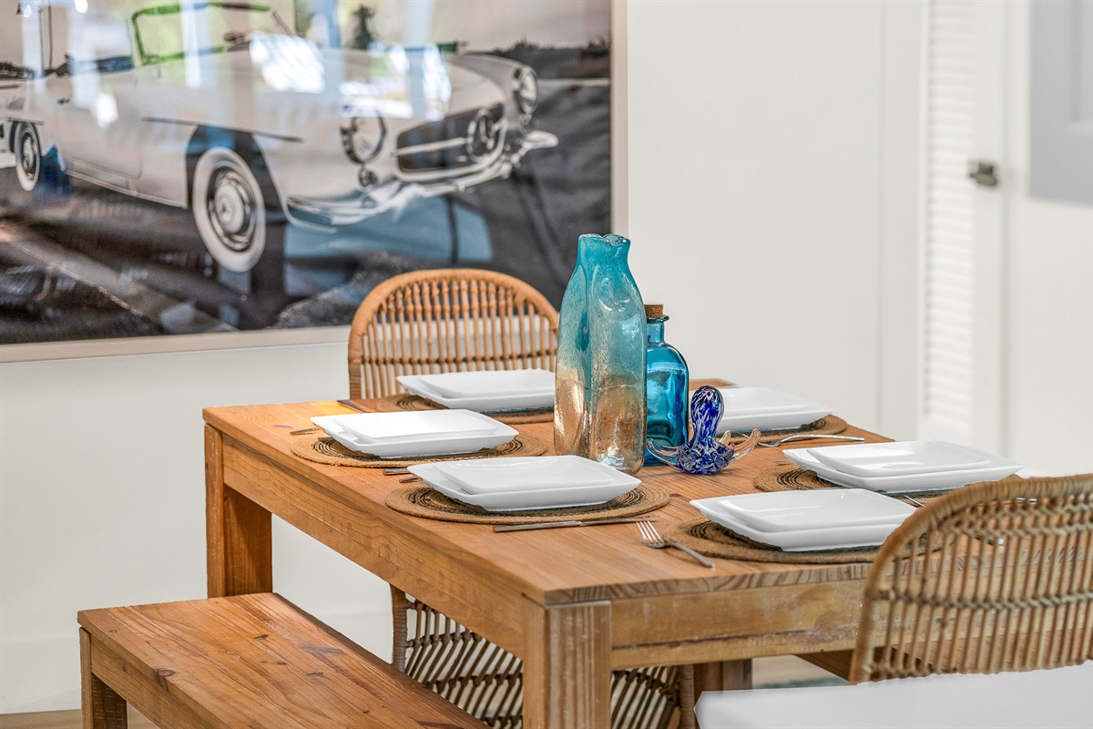 Rustic wood dining accented by chic rattan chairs and a chandelier. Enjoy meals and entertaining in luxurious coastal style
