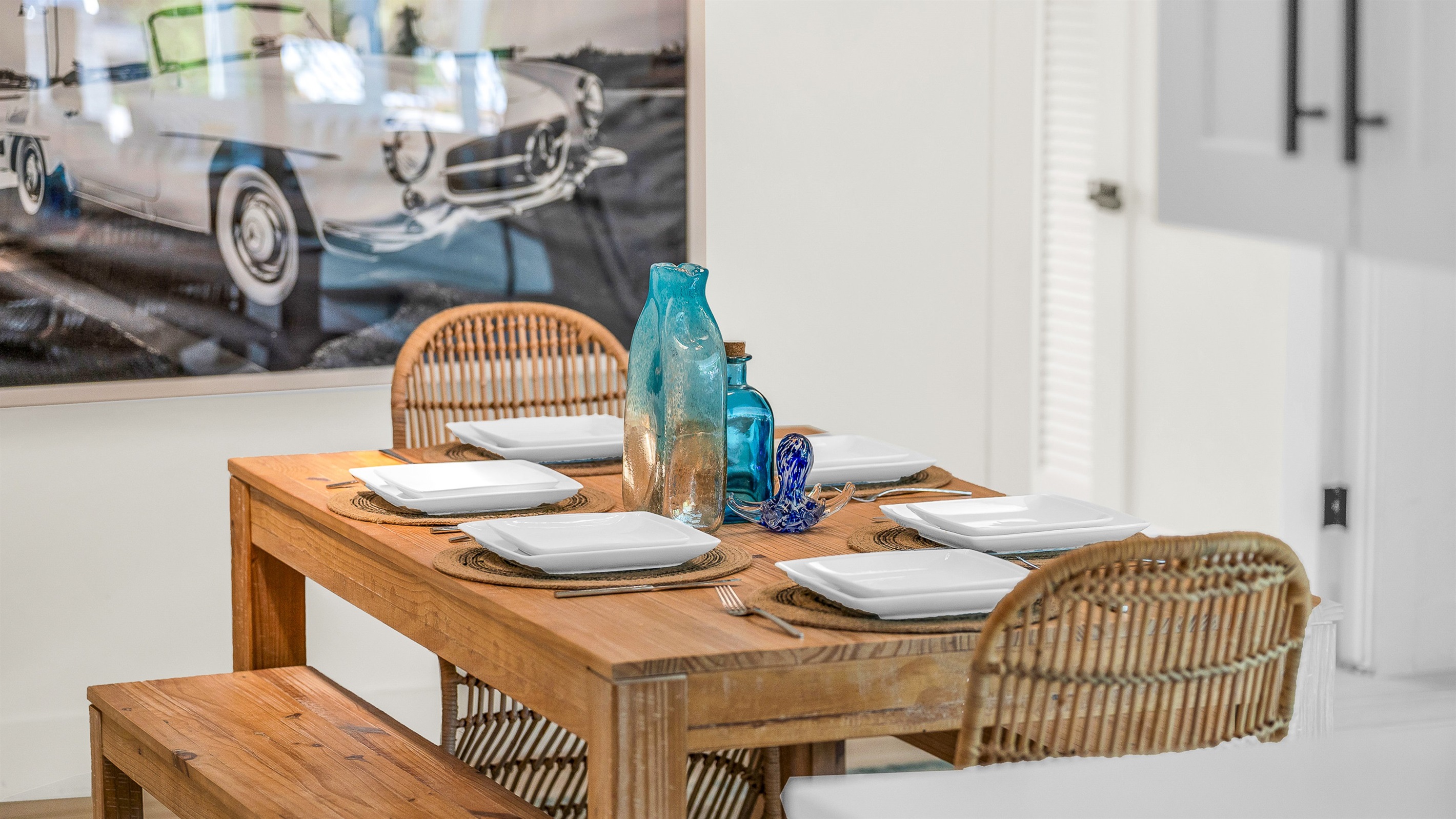 Rustic wood dining accented by chic rattan chairs and a chandelier. Enjoy meals and entertaining in luxurious coastal style