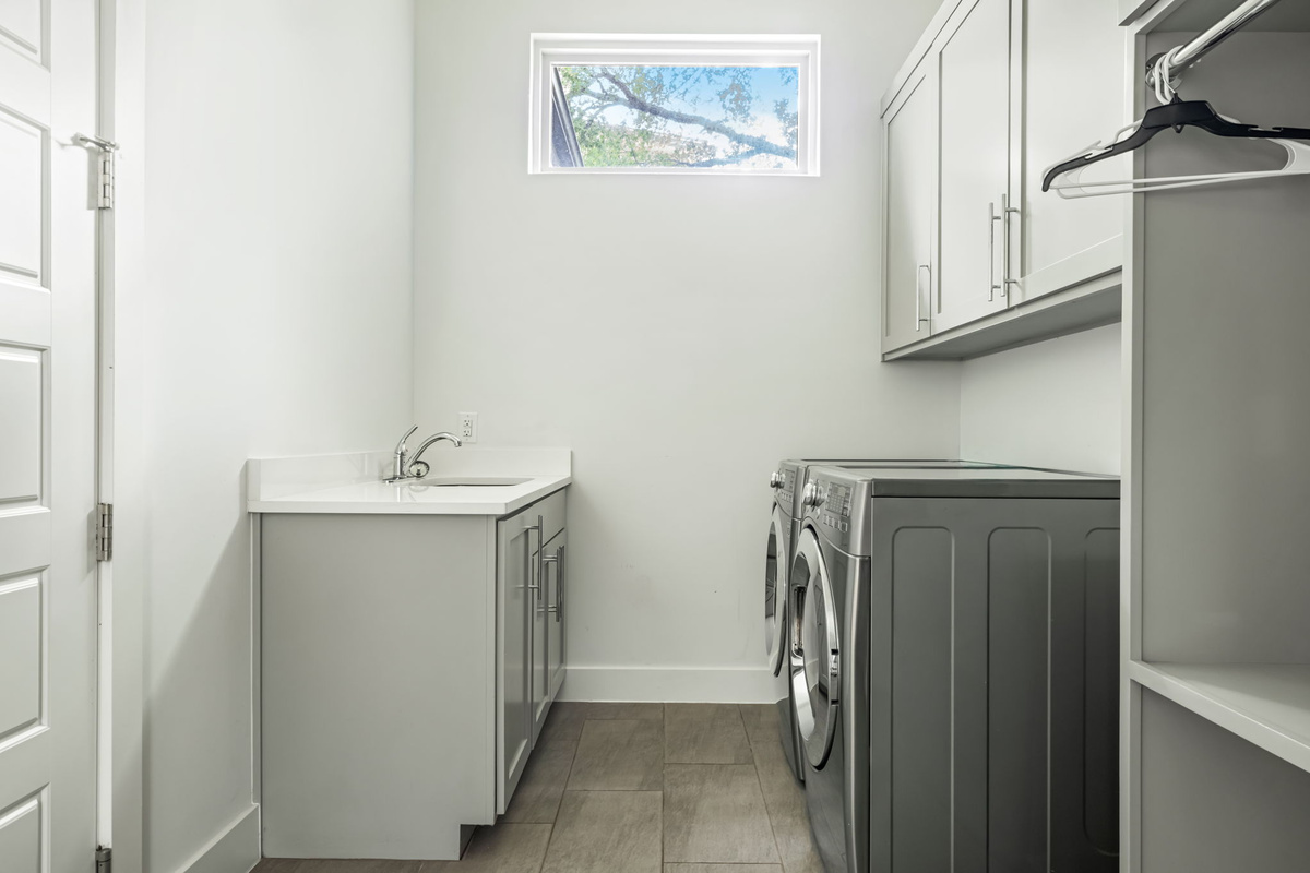 Bright laundry room featuring a utility sink, ample cabinet storage, and full-size washer and dryer — practical convenience for extended stays.