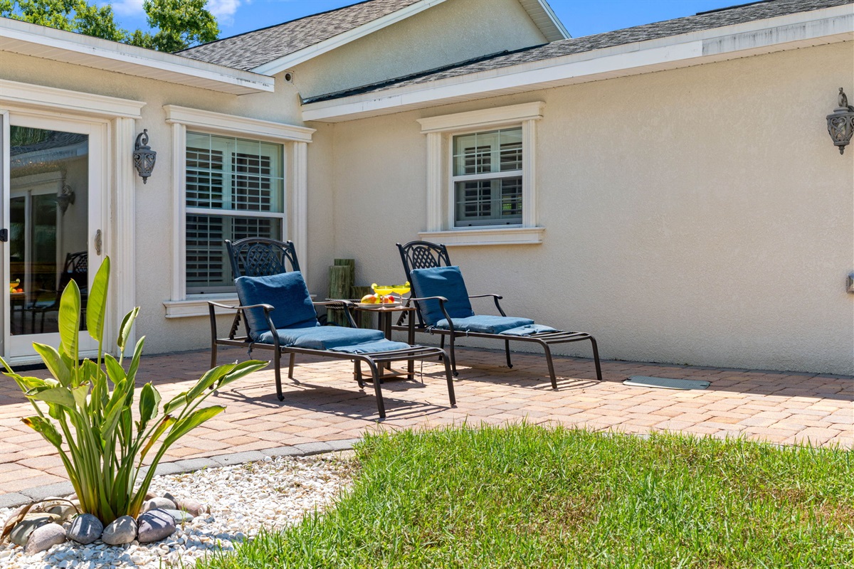 Two inviting chaise lounges with plush cushions sit against the home’s exterior, offering a peaceful spot for sunbathing or enjoying a cool drink.