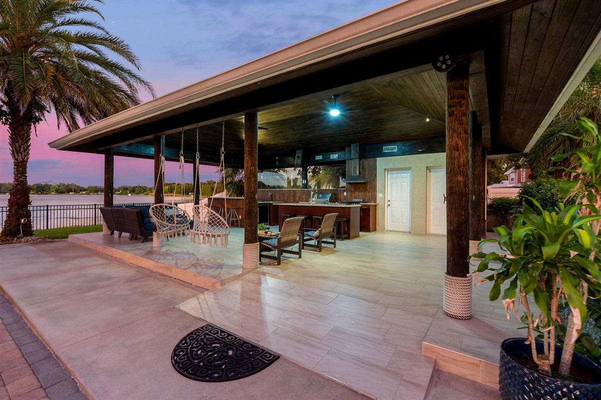 Enjoy gourmet cooking in a fully equipped outdoor kitchen while guests relax in swing chairs and comfortable seating areas overlooking the water.
