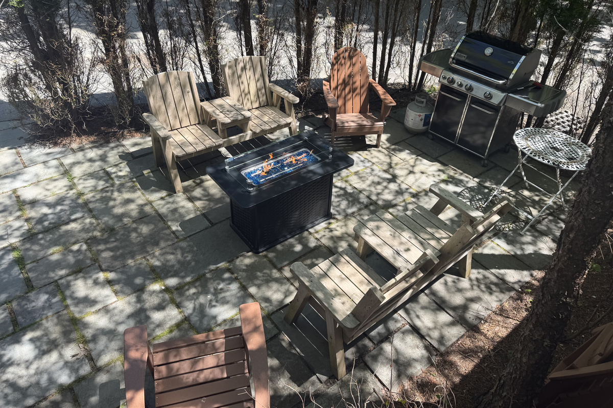 Looking down from the Captain's private bridge onto the stone quarterdeck below. This bird's-eye view shows the entire crew's layout, where the gas fire table, composite Adirondacks, and BBQ grill sit secured behind a wall of privacy trees.
