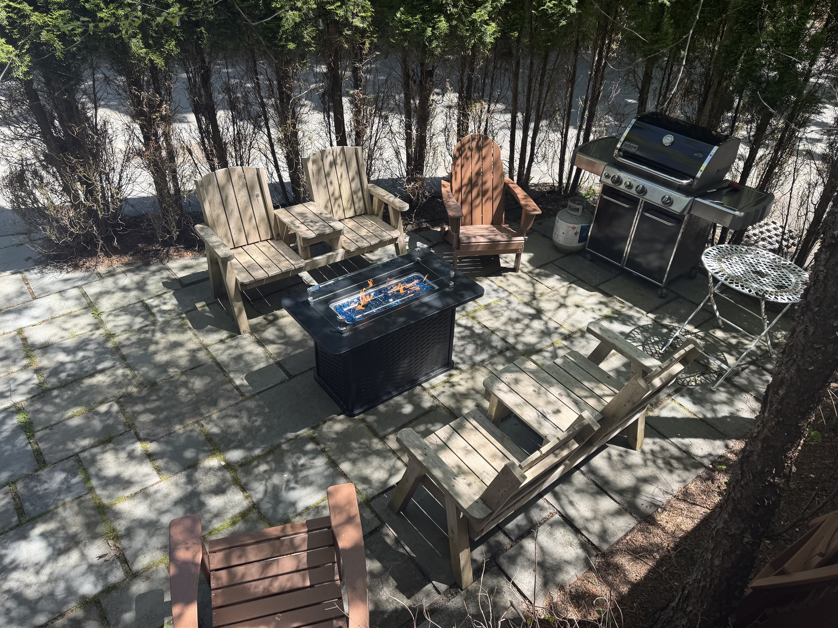 Looking down from the Captain's private bridge onto the stone quarterdeck below. This bird's-eye view shows the entire crew's layout, where the gas fire table, composite Adirondacks, and BBQ grill sit secured behind a wall of privacy trees.