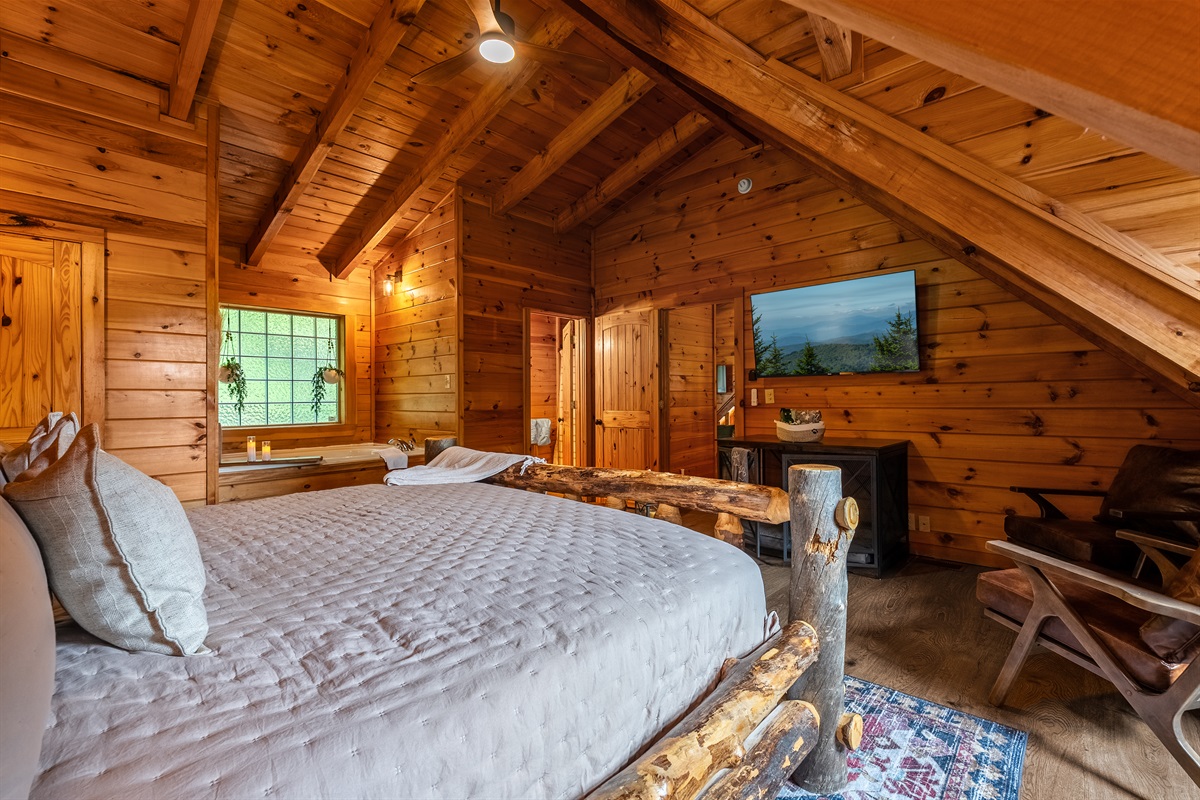Retreat to the spacious upstairs master king suite featuring soaring wood-beamed ceilings, a private seating area, TV, attached bathroom with shower, and a large soaking tub perfect for relaxing after a day exploring the Smoky Mountains.