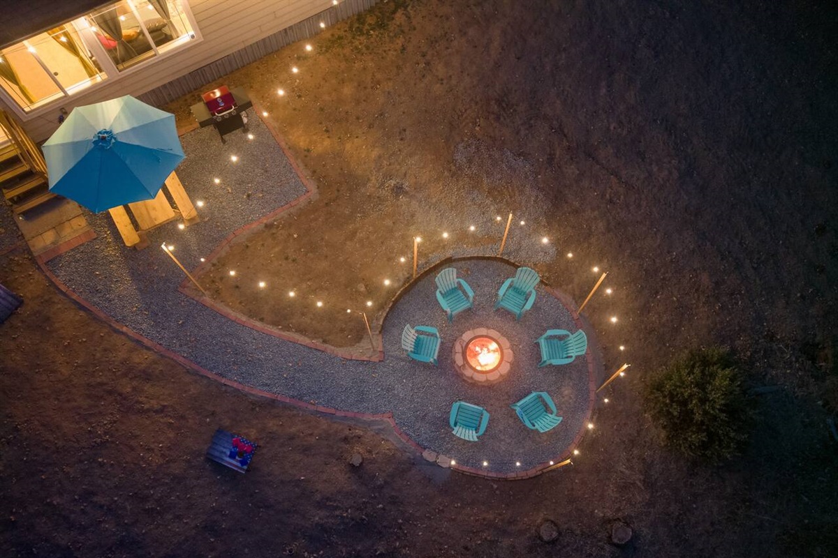 Step into an enchanting outdoor haven where the warmth of a crackling fire pit meets the soft glow of string lights, all under the vast canvas of a breathtaking mountain view. 