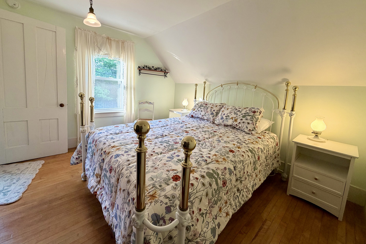 A sun-filled primary bedroom with original 1870s woodwork and a stunning, ornate queen bedframe. Features a brand-new Tempur-Pedic memory foam mattress, offering a serene, ultra-comfortable sanctuary after a day exploring Acadia.