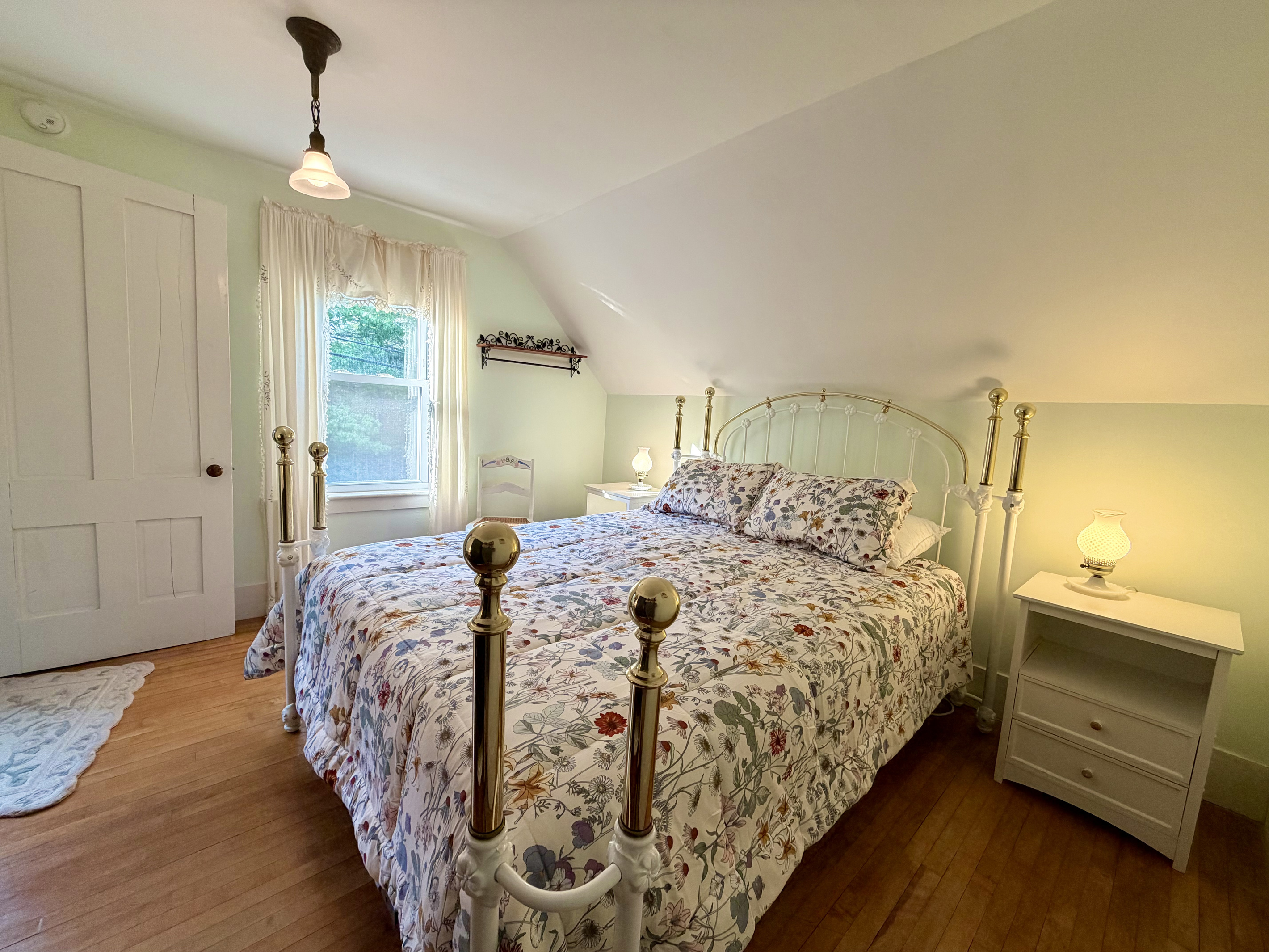 A sun-filled primary bedroom with original 1870s woodwork and a stunning, ornate queen bedframe. Features a brand-new Tempur-Pedic memory foam mattress, offering a serene, ultra-comfortable sanctuary after a day exploring Acadia.