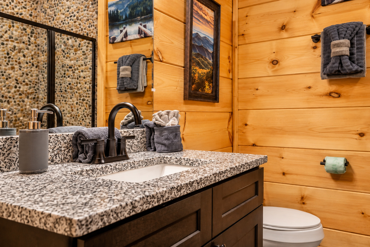 Lakeside and ridgeline art hang above a dark-wood vanity stocked with towels.