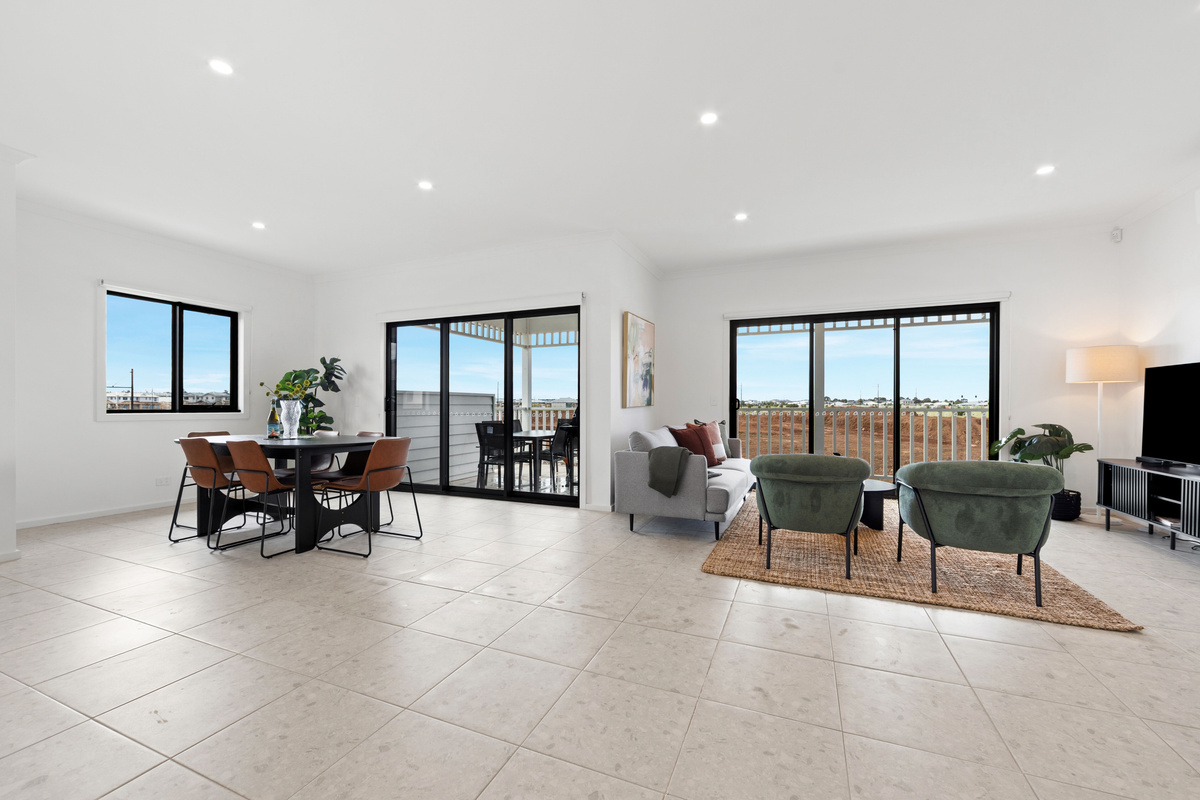 Wide view of the lounge and dining area with the TV, sofa, armchairs and sliding doors out to the balcony.