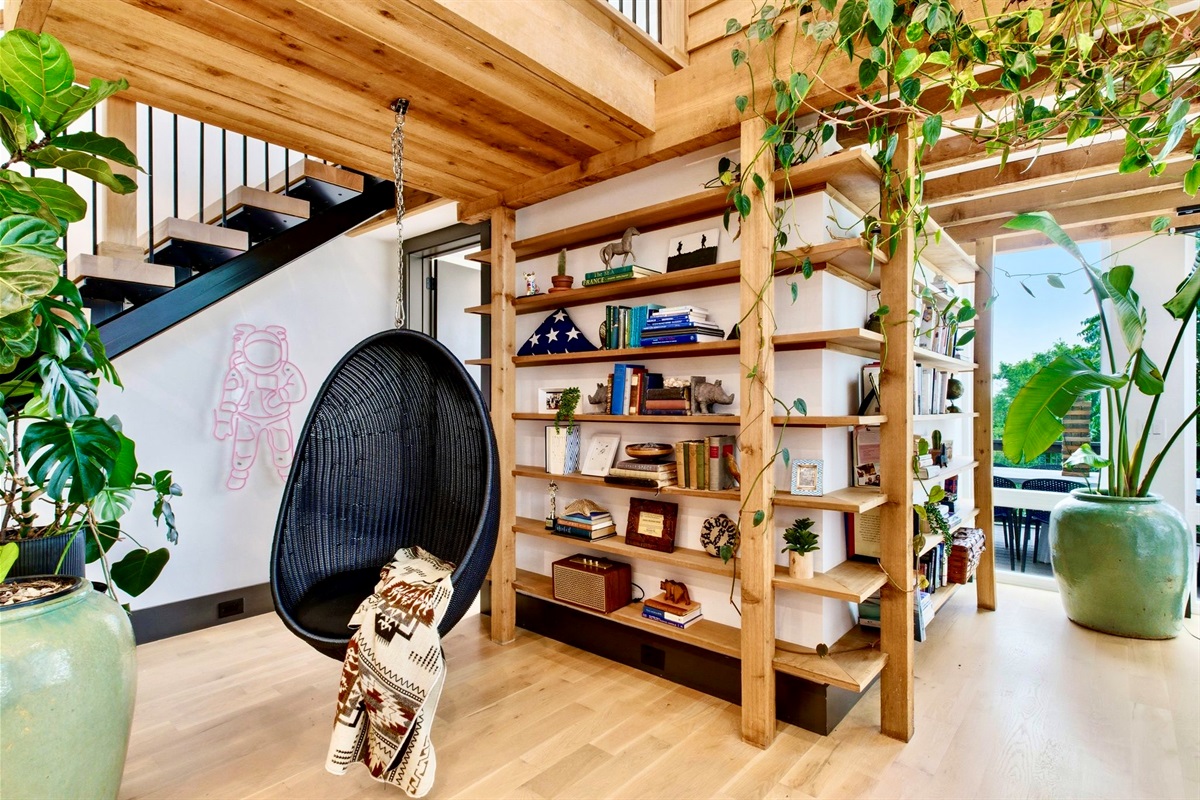 Warm, plant-lined entryway w/ exposed wood shelving & a hanging chair — a welcoming first impression.
