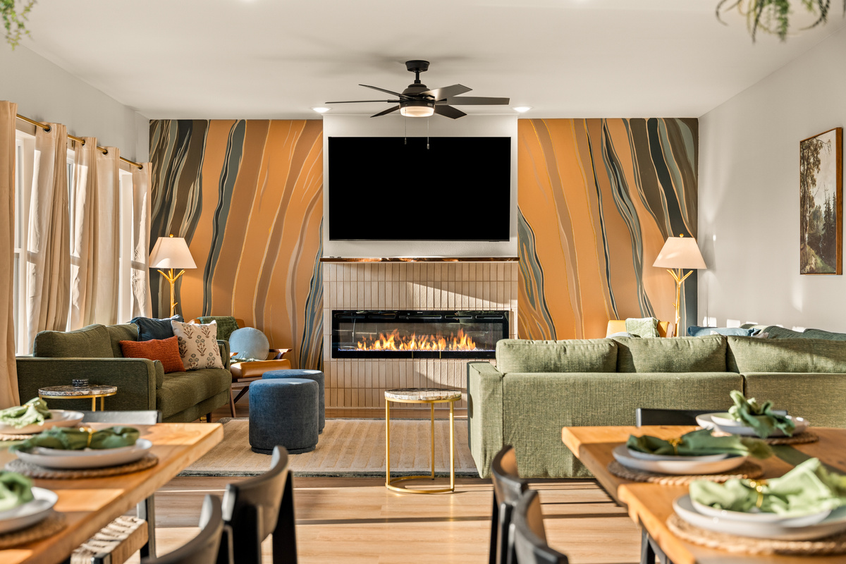 Relax in a beautifully curated living space, where plush olive-green furnishings, warm wood accents, and a dramatic floor-to-ceiling abstract feature wall create a rich, sophisticated backdrop for gathering and unwinding.