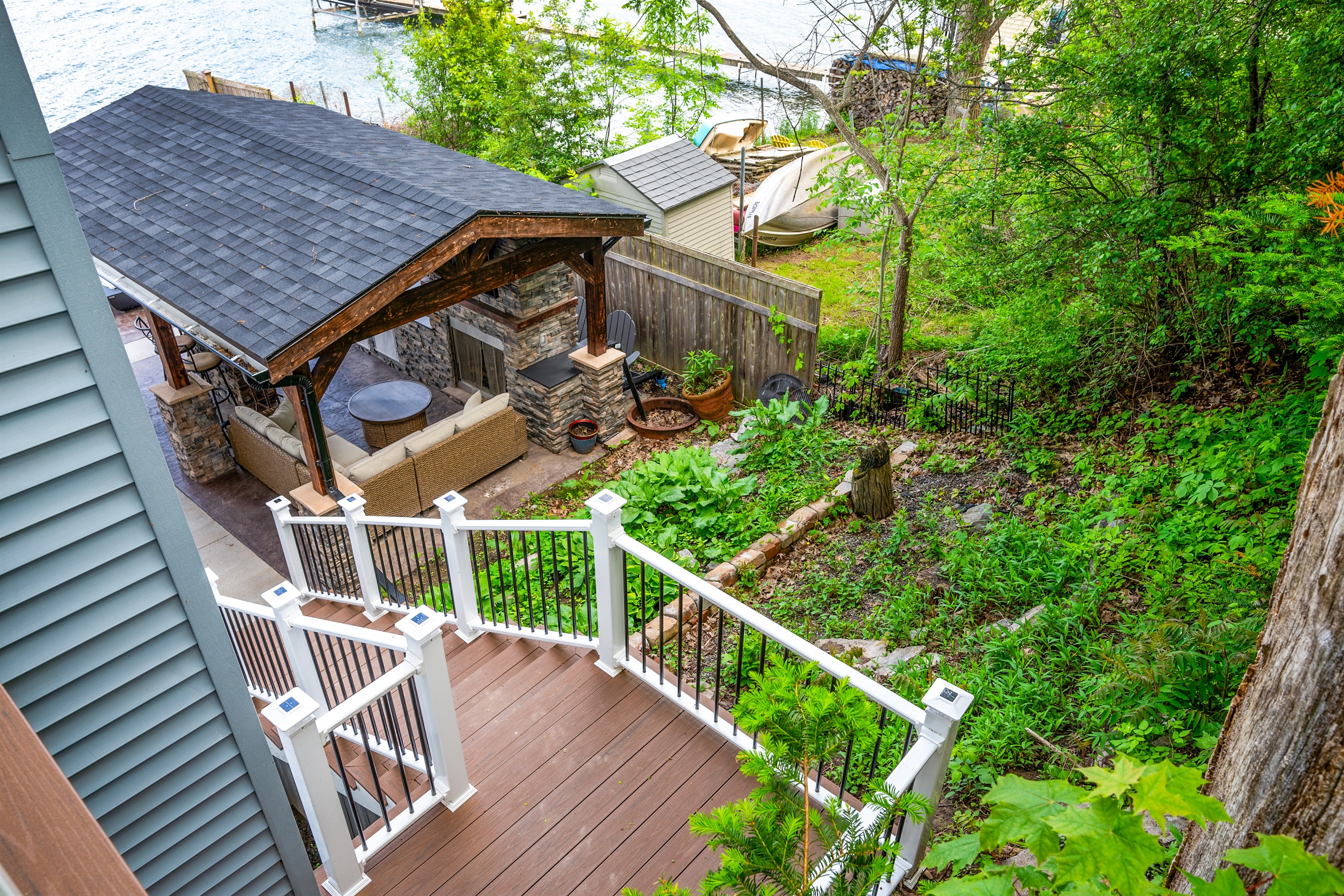 Relax lakeside in this beautiful backyard retreat featuring a covered patio, cozy seating, and lush greenery. 🍃🔥🏡