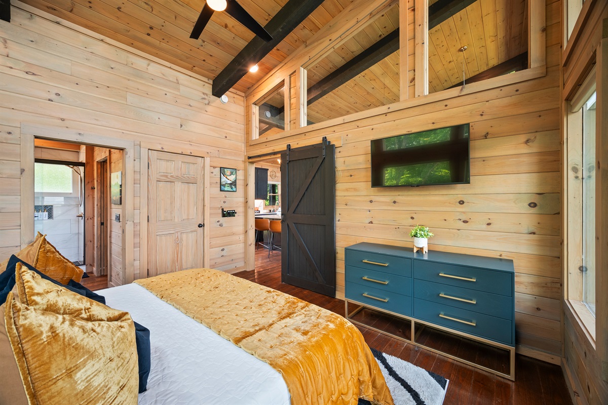 This cozy bedroom features rustic charm with modern touches. Wood-planked walls, black beams, and a sliding barn door that adds character and privacy.