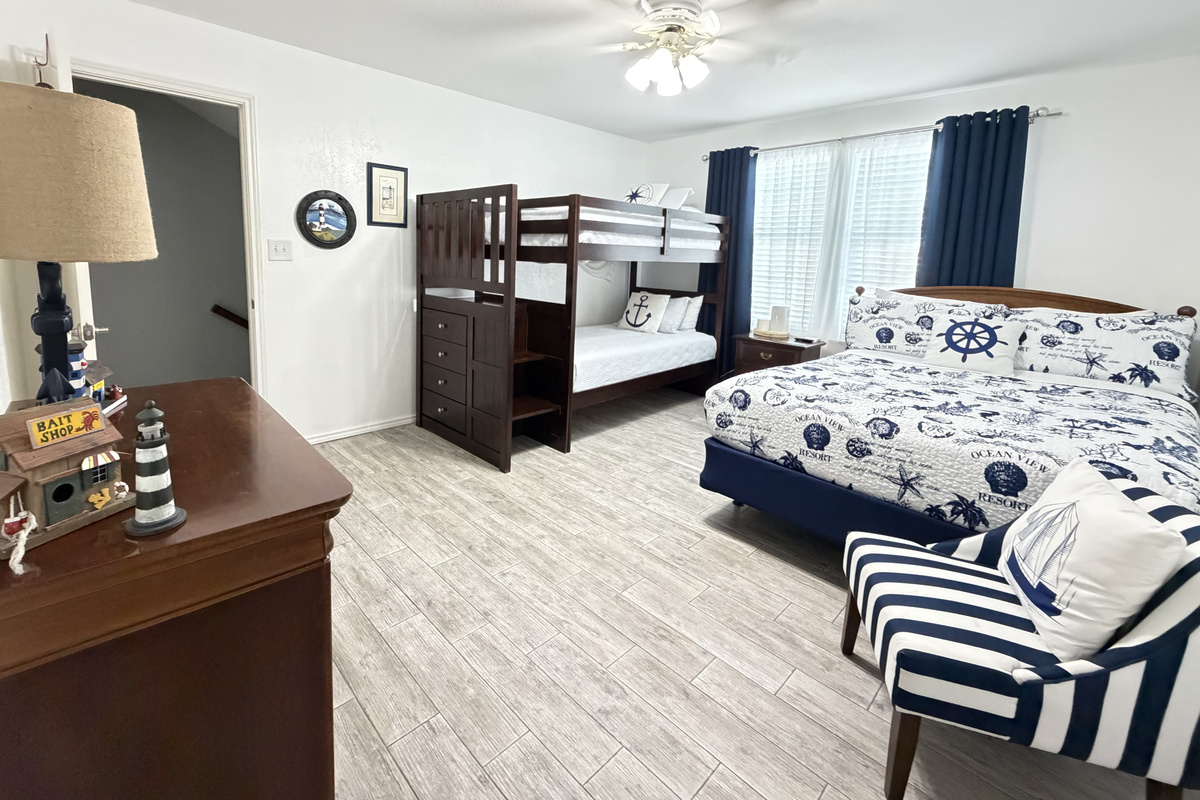 Relax in this charming coastal bedroom featuring two comfortable beds, crisp nautical-inspired linens, and classic navy-and-white accents.  Queen bed and twin bunk beds.