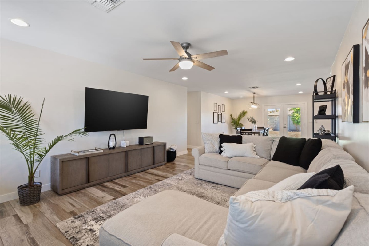 Open living room with large sectional seating, ceiling fan, perfect for gathering! Black storage box contains children's toys.
