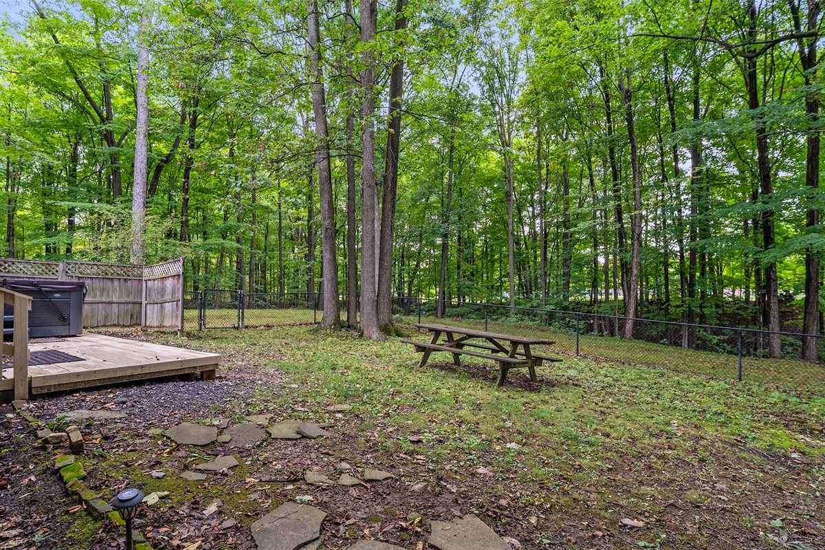 Relax in the private, fenced backyard surrounded by tall trees, complete with a picnic table for outdoor meals and space to soak in nature.