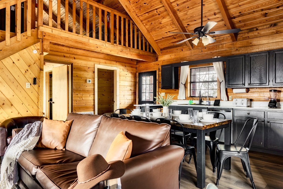 Inside a cabin, a kitchen, living room, and dining area are beautifully arranged for a homely and perfect gathering. 