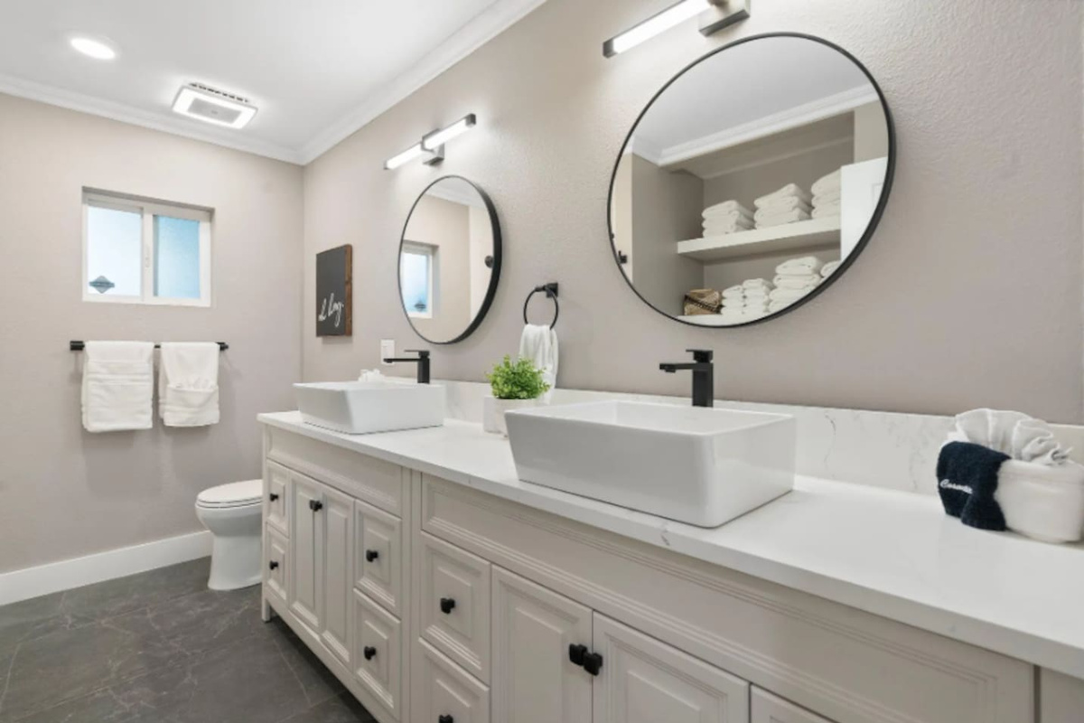 A long dual vanity with vessel sinks gives this bathroom plenty of room to spread out, while round mirrors and stacked fresh towels add a spa-like finish. Natural light from the window keeps the space feeling bright throughout the day.
