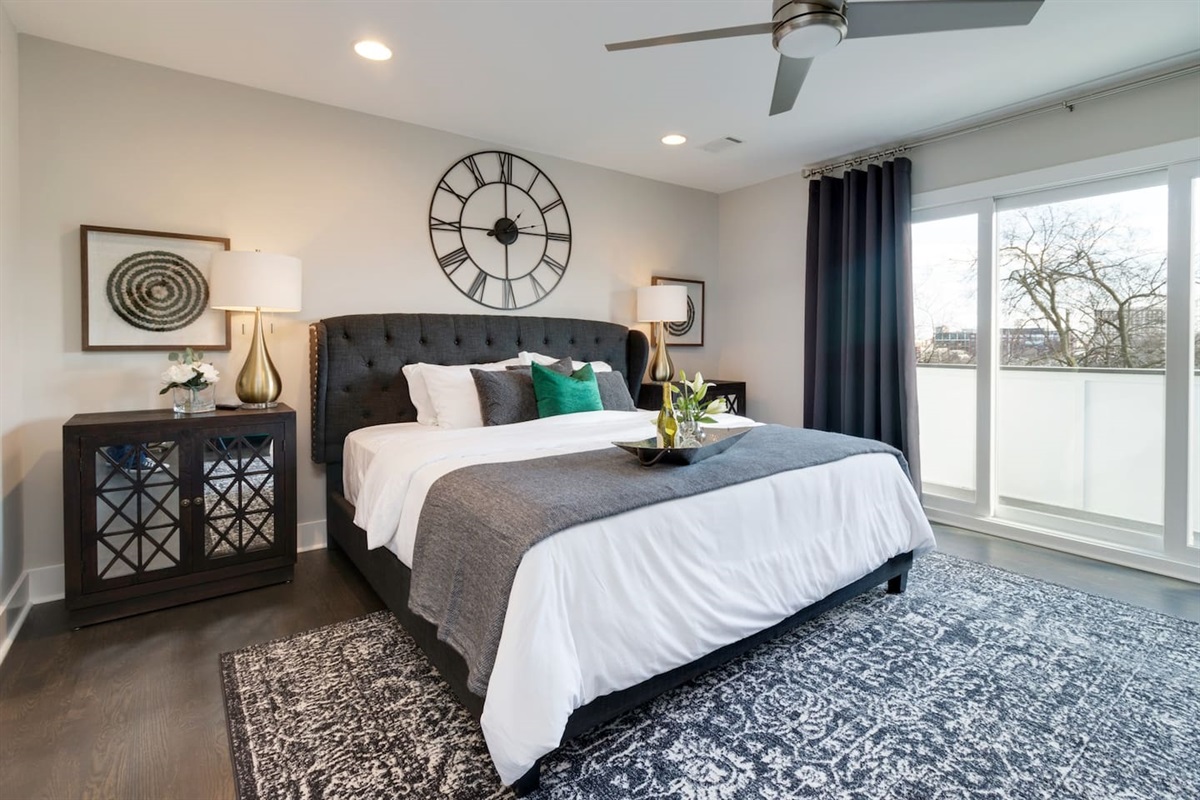 - King size bed with a tufted headboard, layered pillows, and bold wall decor statement - Blackout curtains and glass balcony doors offer both privacy and natural light - Designer nightstands, soft area rug, and ceiling fan complete the tranquil retreat