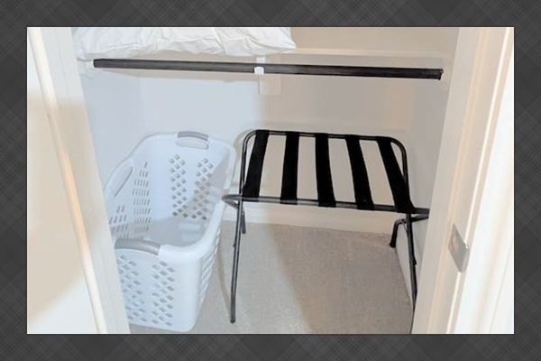 Extra storage space in the closet that is stocked with hangers, luggage rack, and laundry hamper. 
