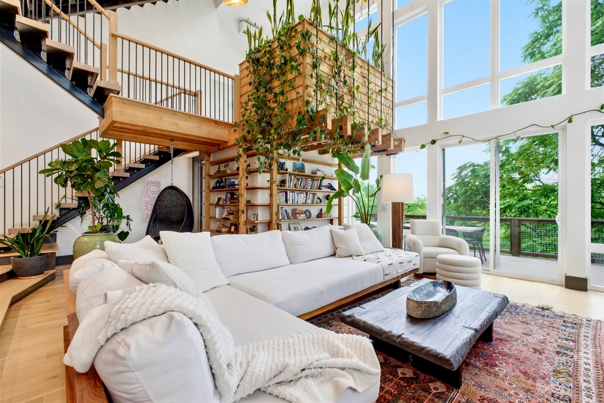 Breezy upper-level lounge w/ white sectional, trailing plants & treetop light pouring in.
