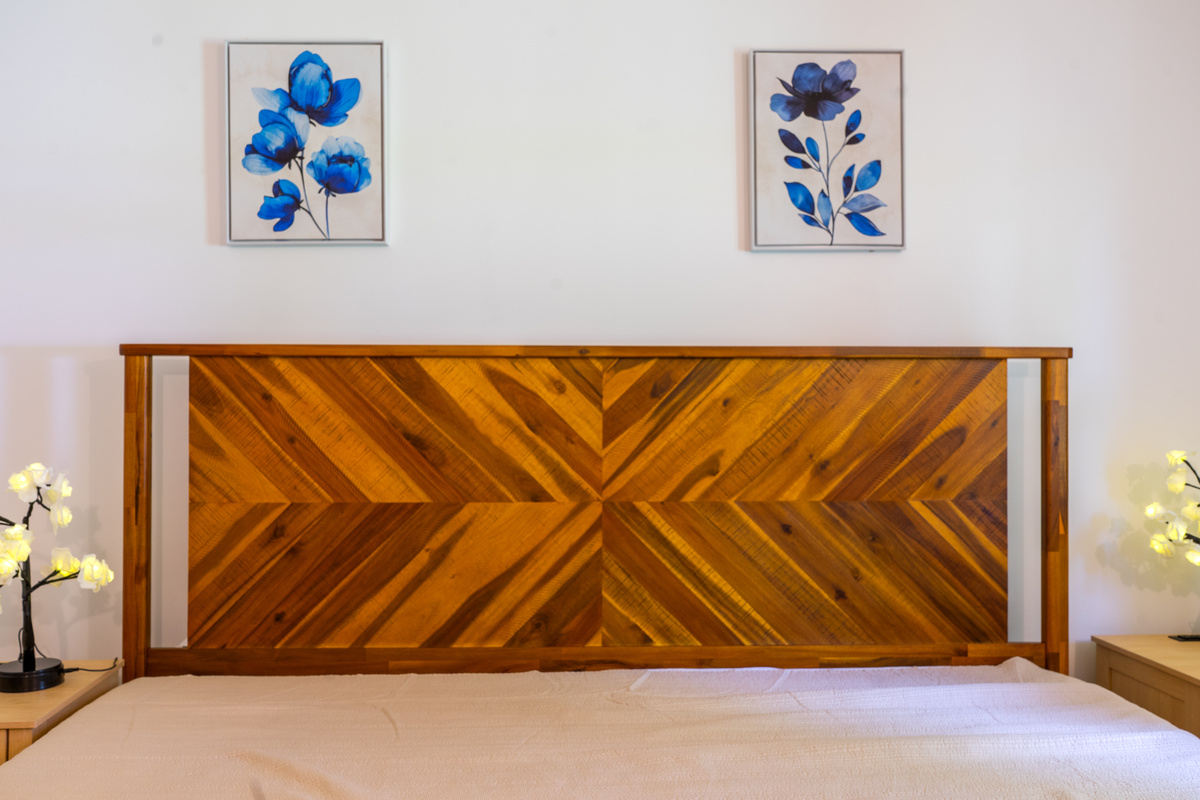 Admire the beautiful craftsmanship of the king bed's geometric chevron headboard. Flanked by matching wooden end tables with unique glowing floral branch accent lamps, this balanced setup highlights the thoughtful design of the flower room.