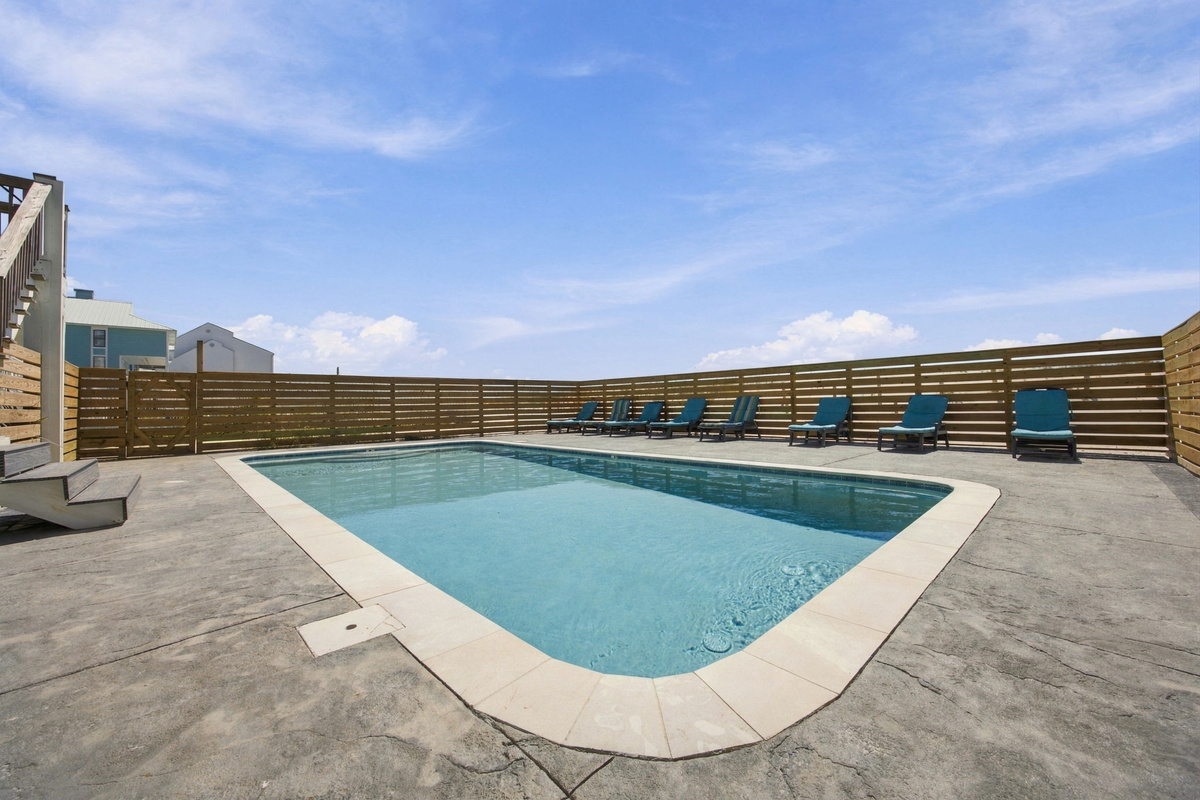 Private outdoor pool with crystal-clear water, lounge chairs, and a spacious deck designed for sunny beach vacation days.