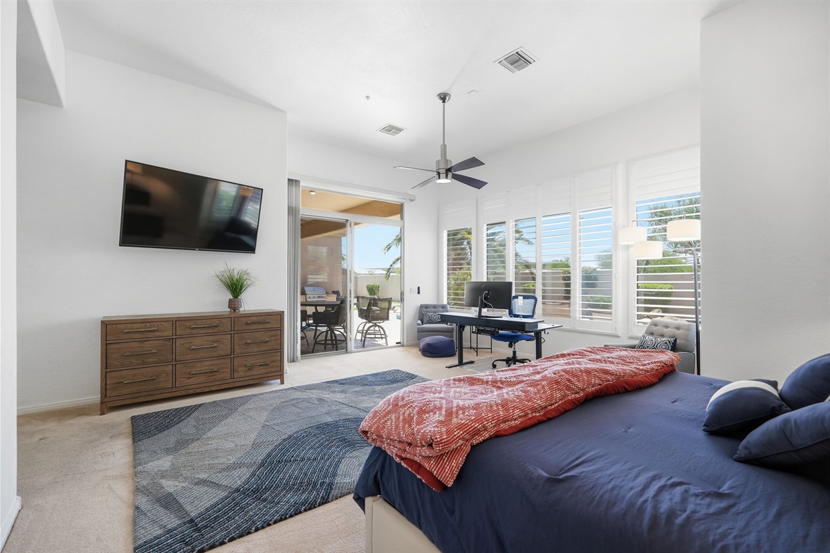 Well-appointed primary bedroom with ceiling fan, patio access, and TV.