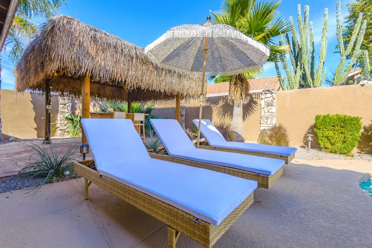 Poolside lounge area with seating, umbrella shade, and a tiki-style bar for sunny outdoor downtime.