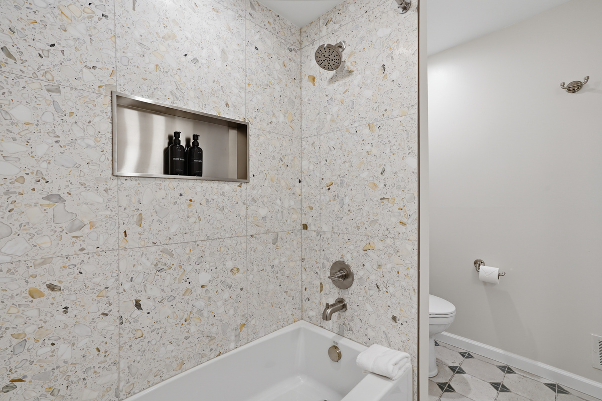 Spa-like bathroom with stone tile, built-in niche, polished chrome fixtures, and a deep soaking tub. Bright, modern design with clean lines and a calm, upscale, hotel-inspired feel.