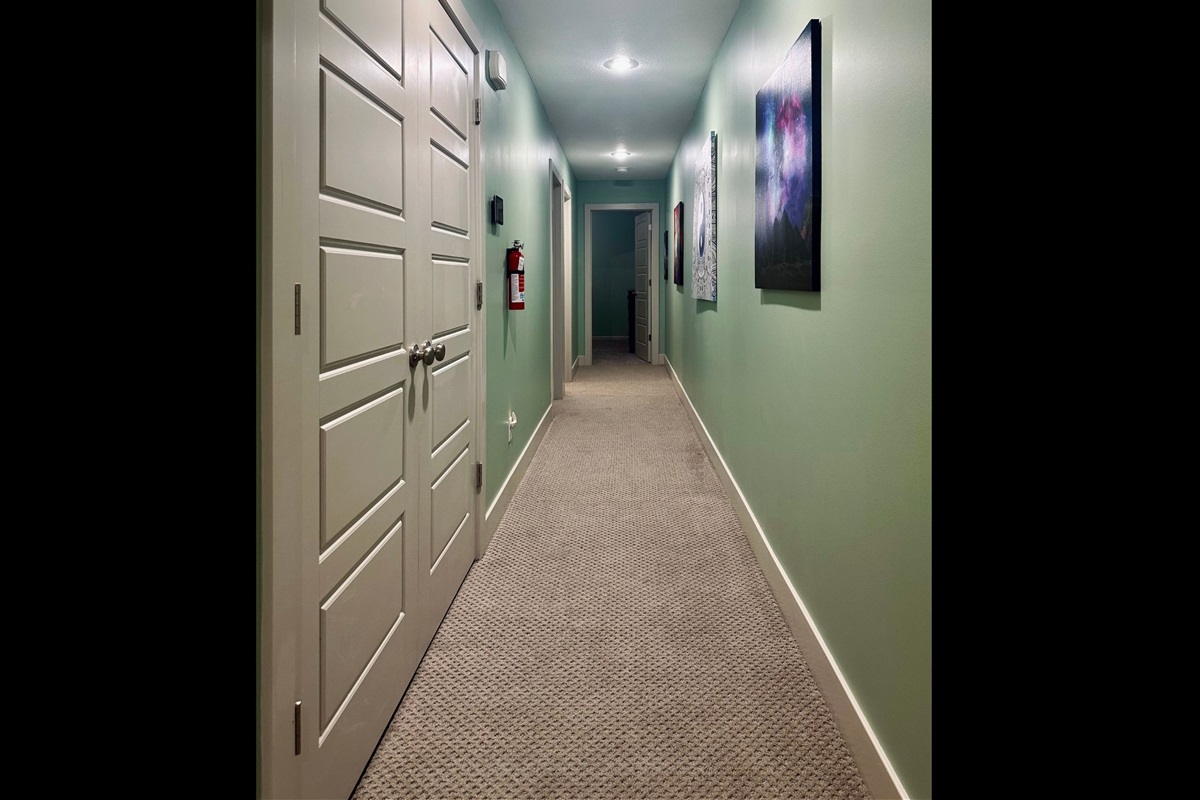 Upper-level hallway facing east toward Bedrooms 2 and 3, with double doors on the left concealing the conveniently located laundry area.