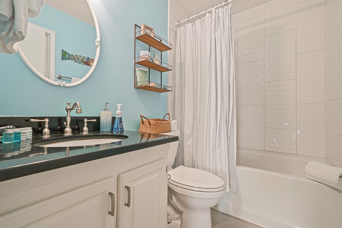 Tub/shower combo with honeycomb tile accent, dark granite vanity, and rustic floating shelves. Two full bathrooms for up to 6 guests.