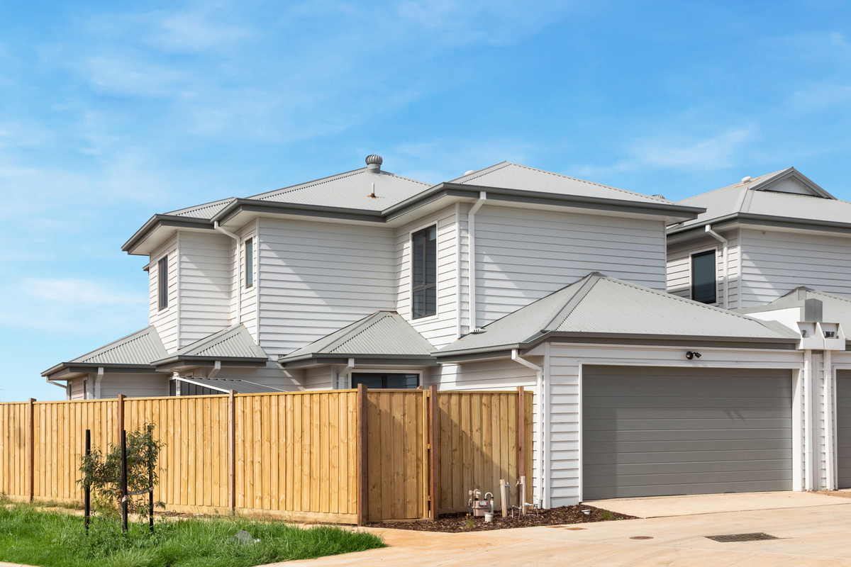 Street view of the two-storey townhouse with its garage, timber fencing and young landscaping.