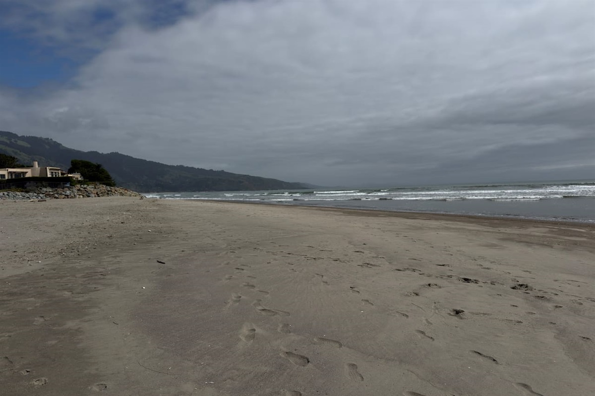 Wide sandy beach with waves and mountain views.

