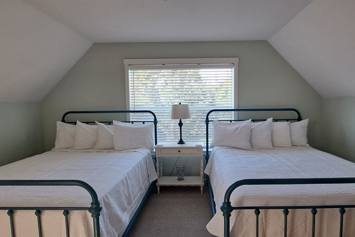 Unwind in the family suite, featuring two queen beds with luxury mattresses and sea-glass-colored walls that perfectly capture the relaxed charm of coastal living.