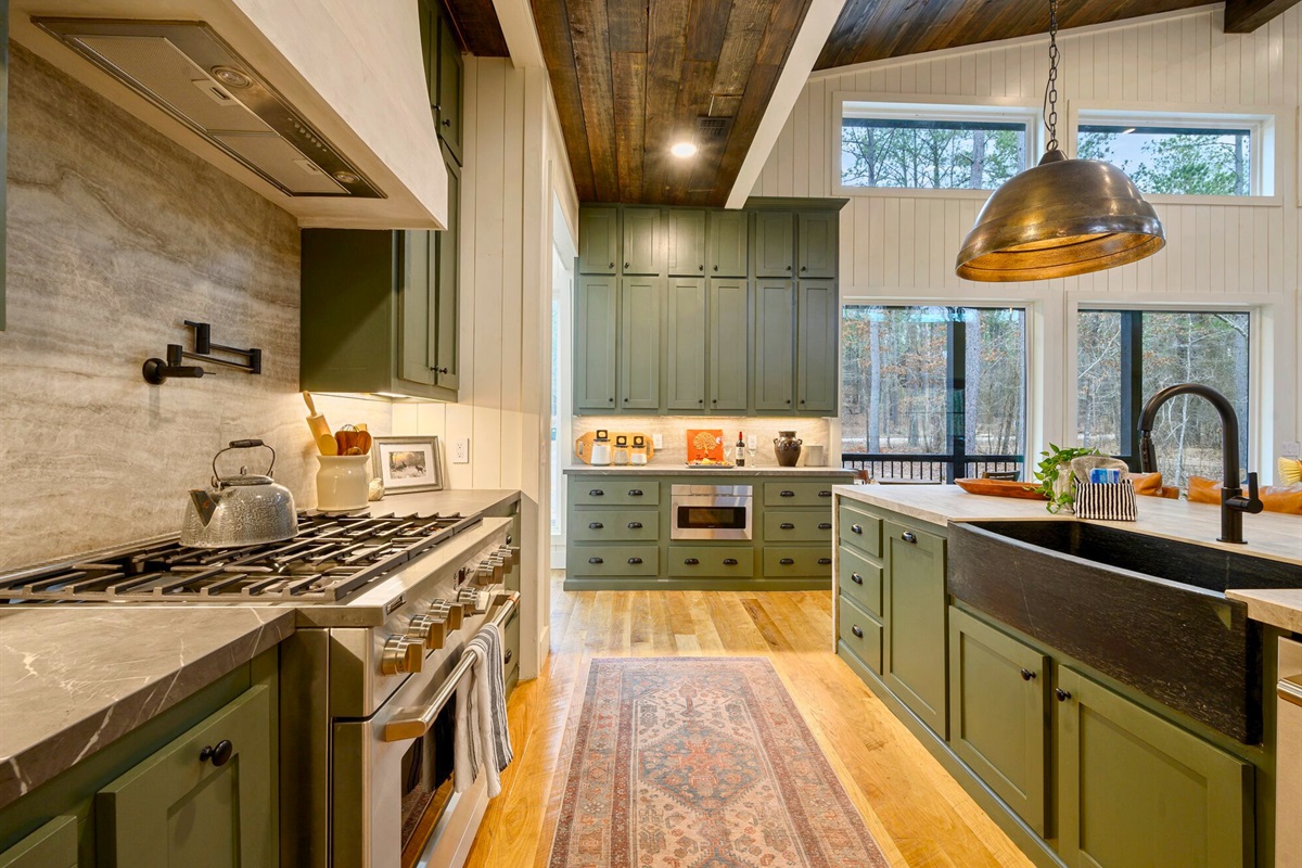 Green cabinetry adds a warm pop of color to the kitchen, paired with sleek appliances and plenty of prep space.