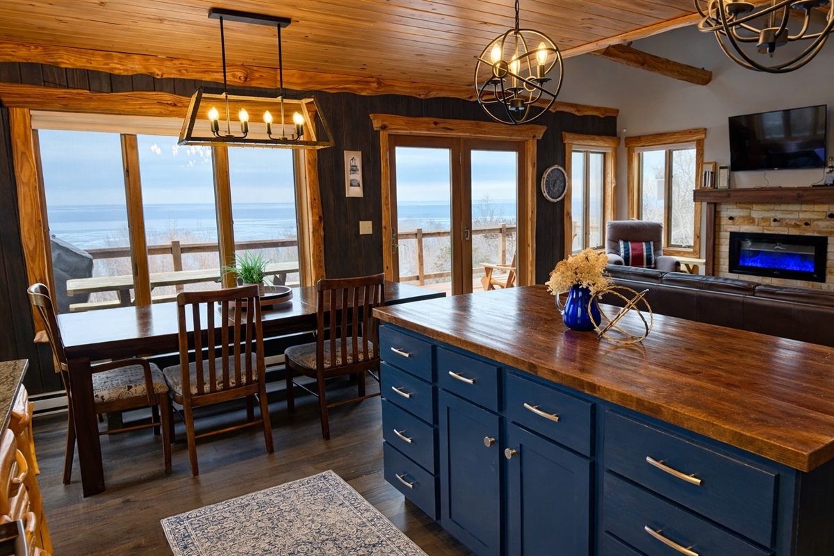 Kitchen to living view with the island front and center, fireplace, TV, and dining table all framed by big windows and Lake Superior views. The perfect spot to prep dinner and gather.