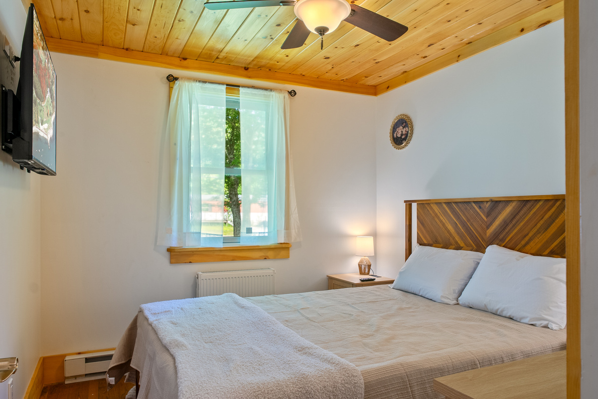 Sleep soundly in the peaceful queen guest bedroom featuring a beautiful chevron-patterned wood headboard. This cozy retreat is well-appointed with crisp white bedding, a wall-mounted flat-screen TV, and an overhead lighted ceiling fan.