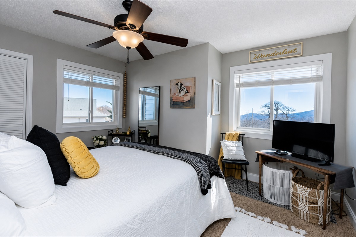 Bedroom with a mountain view. Furniture configuration has been updated to include wall mounted TV, with the table and chair under the window for a dedicated work space.
